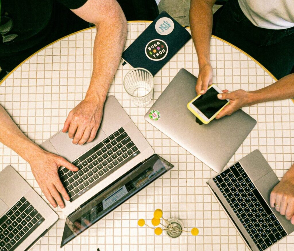 Top view of a team collaborating with laptops, phones, and notes in a modern office.