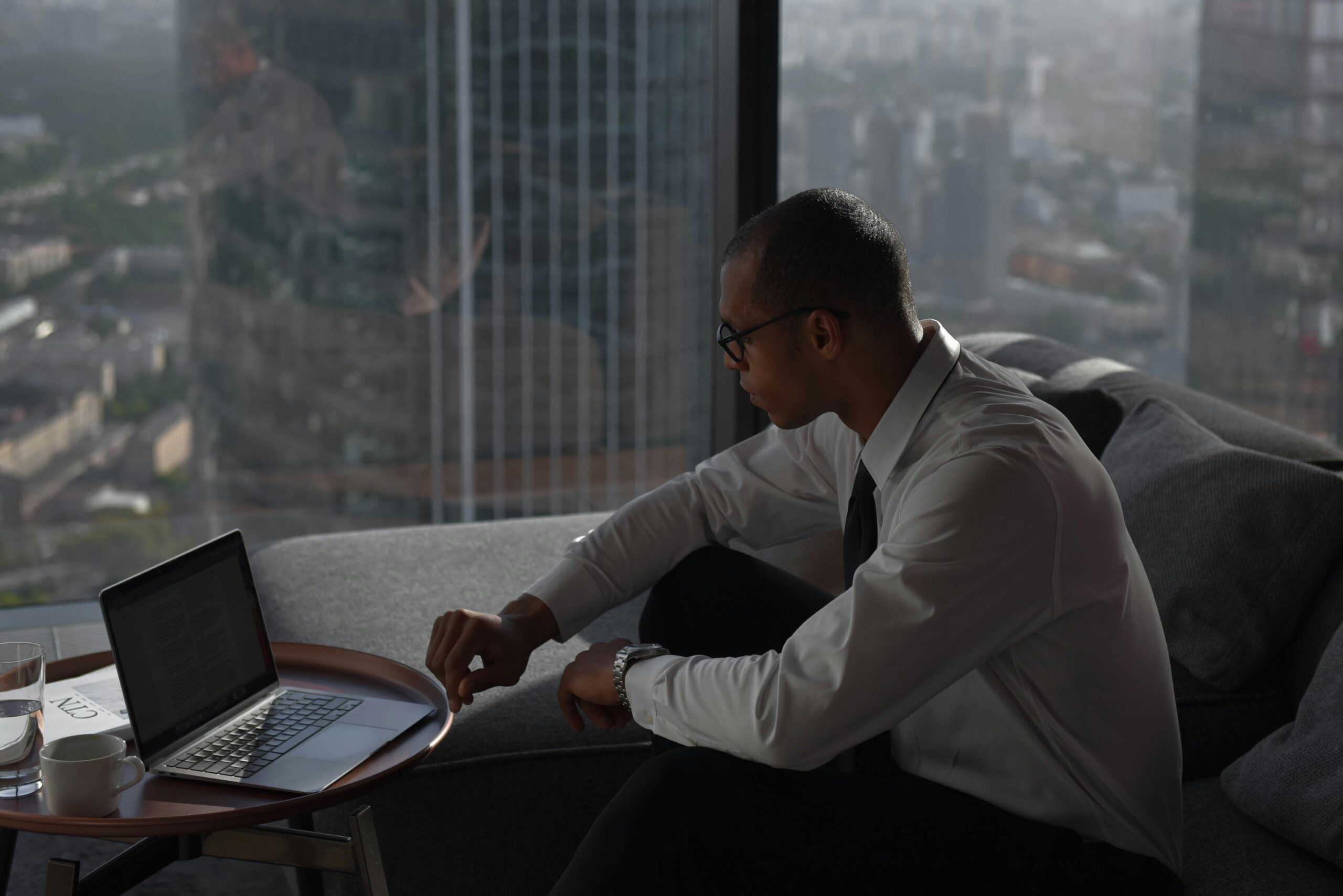 Businessman working on a laptop in a modern office setting with a panoramic city view.